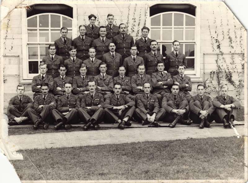 A posed group of 31 men in RAF uniforms outside of a white building with windows