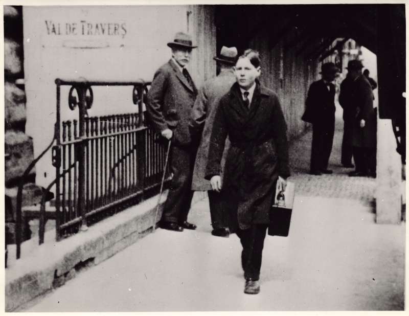 A teenage Leonard Cheshire carrying a briefcase down a street with people in the background