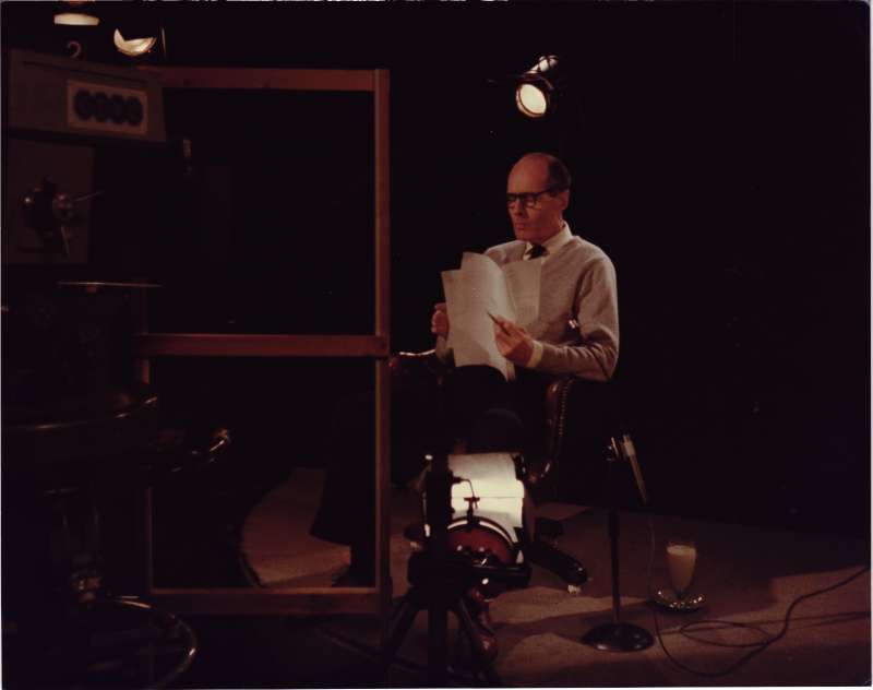 Leonard Cheshire looking through a script, sitting in a director's chair in a film recording studio