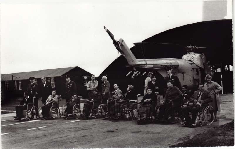 Several people in wheelchairs and others standing in front of an RAF helicopter at RAF Odiham