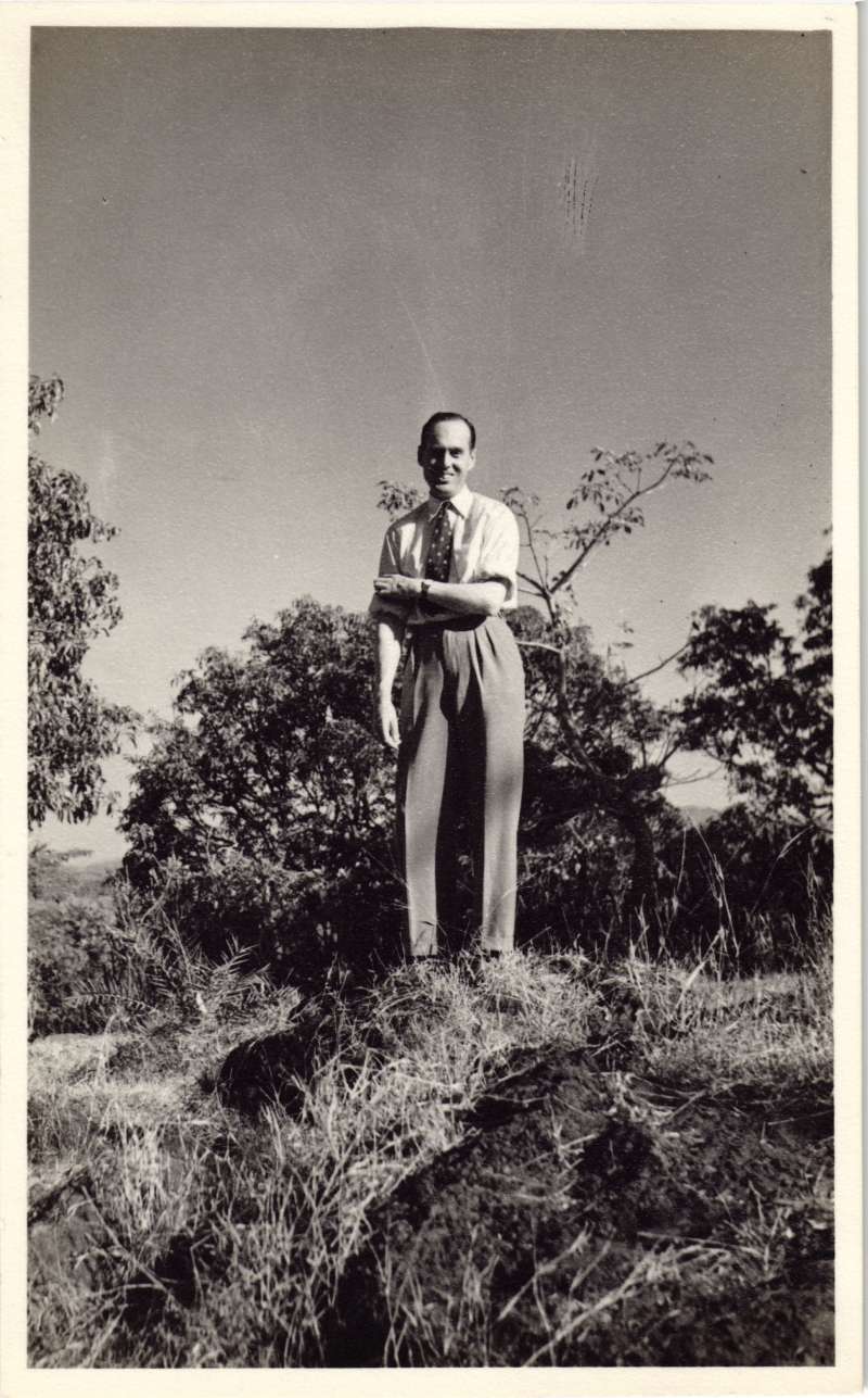 A young Leonard Cheshire standing on a lawn in front of several bushes