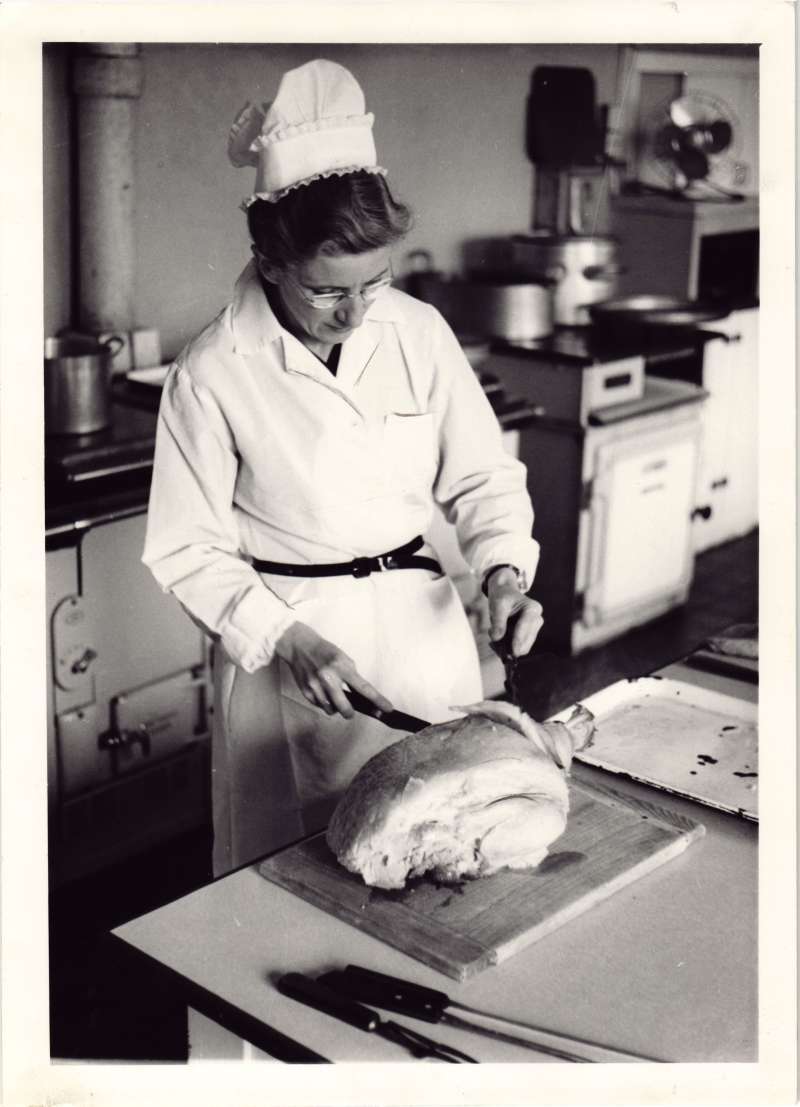A woman in chef's whites and hat carving a turkey in the kitchen