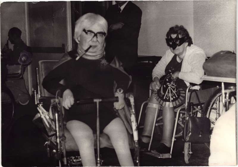 A man in fancy dress in a wheelchair and a woman wearing a mask and holding a witch's hat