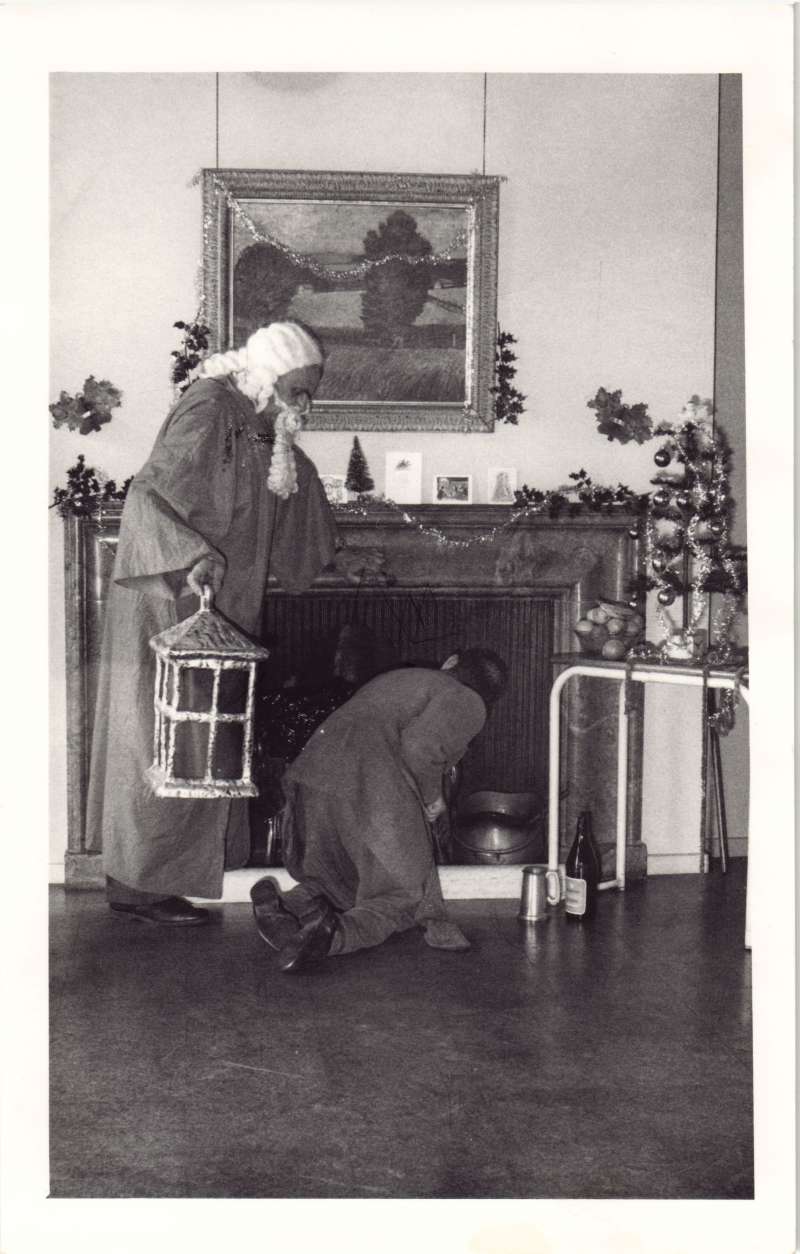 A man kneeling looking up the chimney with a man dressed as Father Christmas standing behind