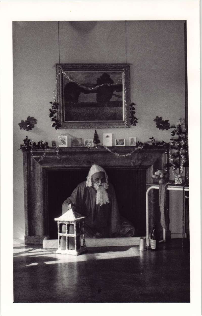 A man dressed as Father Christmas sat in front of a decorated fireplace
