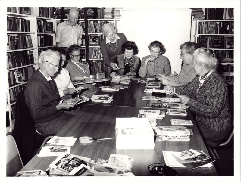 A group of people around a table in a library sorting through piles of Christmas cards