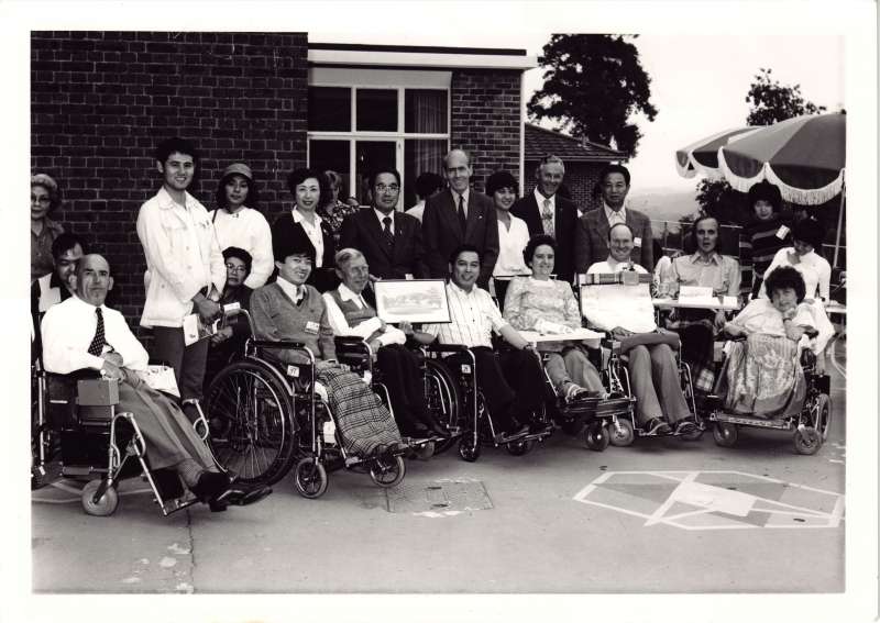 A posed group of people standing and in wheelchairs outside the Le Court building