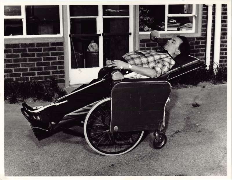 A man in a specially adapted horizontal wheelchair outside a brick building with windows