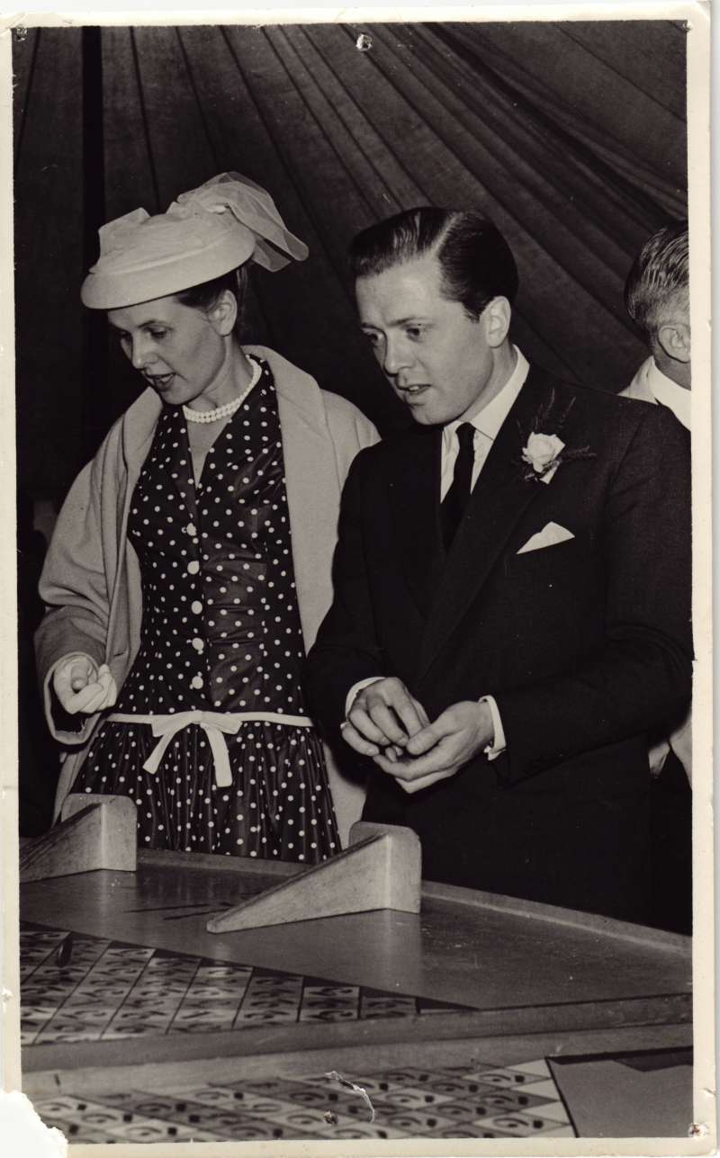 A man in a smart suit and a woman in a polka dot dress playing roll a penny at a fete