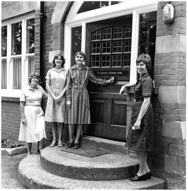 Four women standing on the steps of St Cecilia's home, two in nursing uniforms
