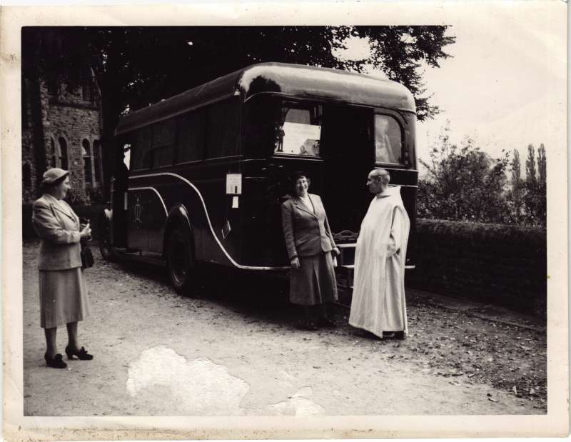 Two ladies standing next to a bus talking to a monk