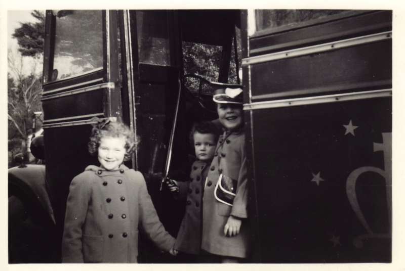 Three children holding hands standing on the steps of a bus