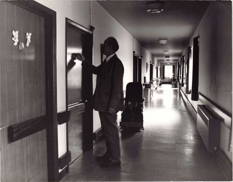 Man knocking at a door on a long corridor.