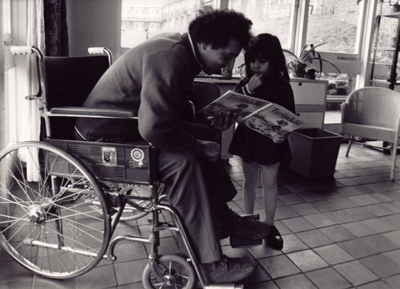 Man in a wheelchair reading a story to a young girl.