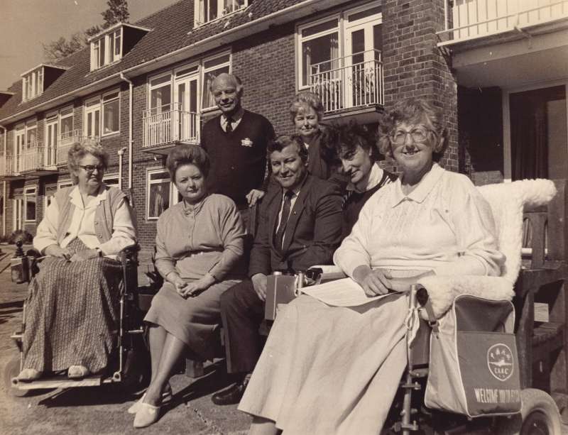 Two female residents in wheelchairs and five other people in a posed photo on the terrace at Le Court