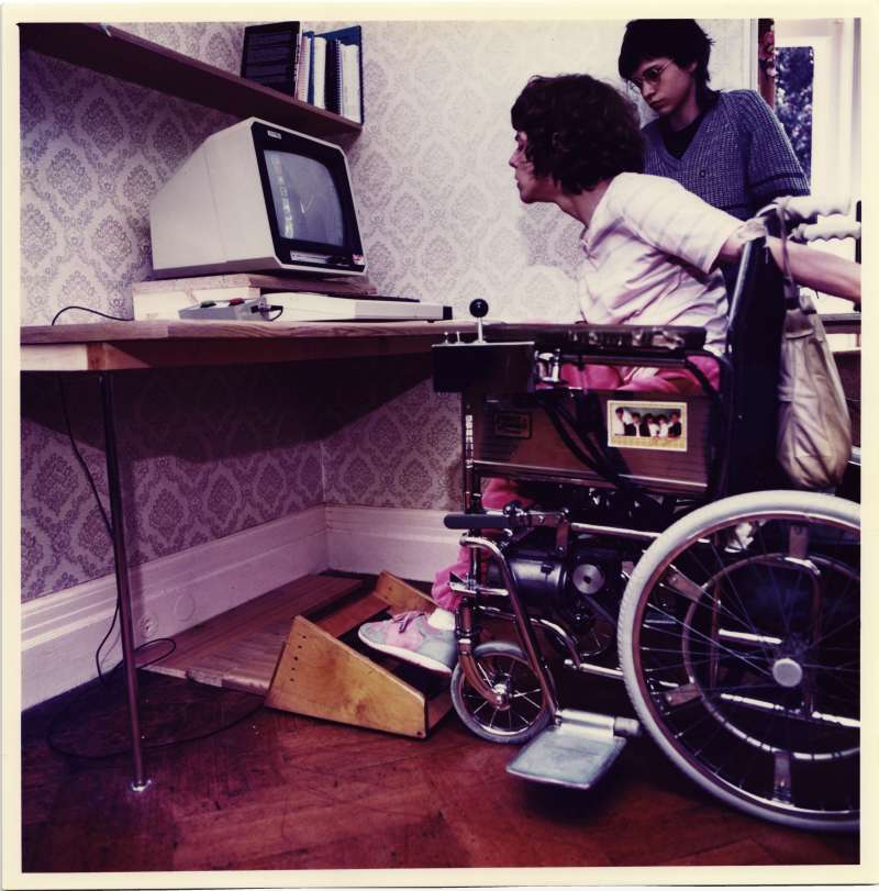 Woman in a wheelchair using assistive technology with her feet to operate a computer