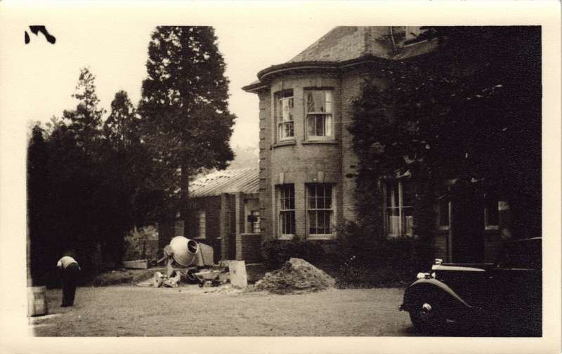 Photo of an older building with a cement mixer in front and a man bent over working