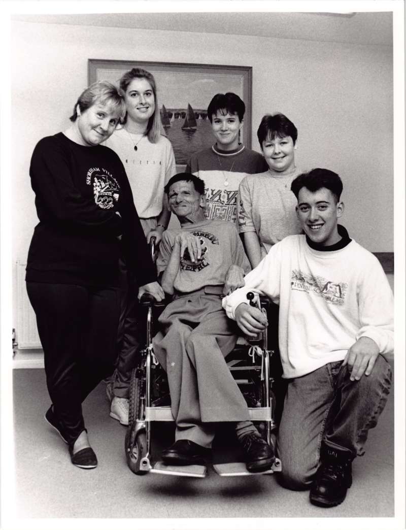 Indoor group photograph of a man in a wheelchair surrounded by five others