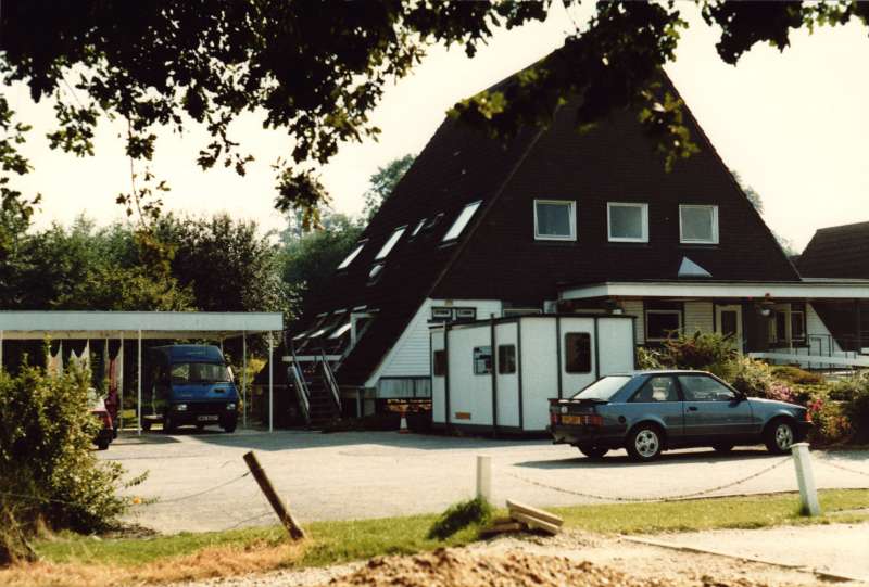 Colour photograph of the exterior view and driveway with cars at Chipstead Lake