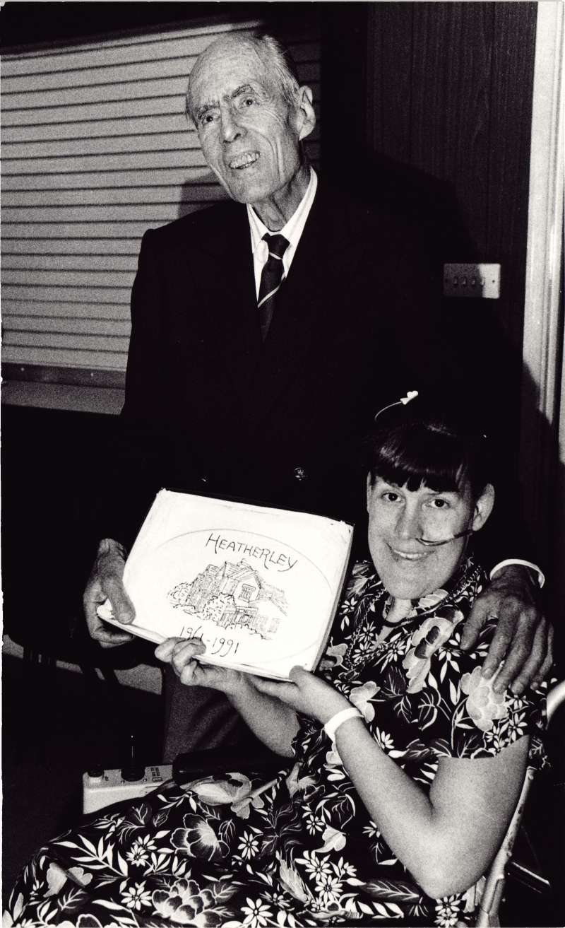 Young woman in a wheelchair in a floral dress holding a plaque jointly with Leonard Cheshire