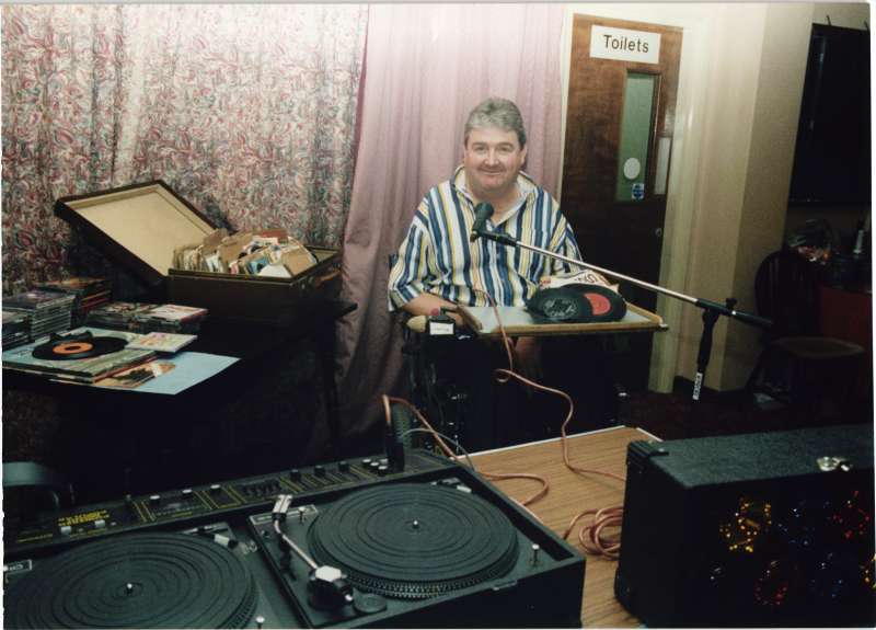 Man in a wheelchair surrounded by vinyl records and record-playing equipment