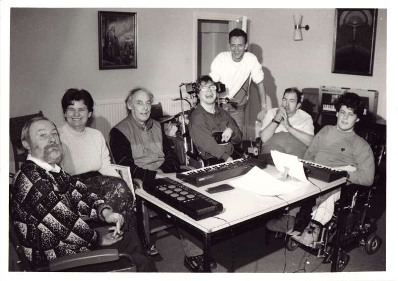 Group of seven people, many in wheelchairs sat around a table with music keyboards