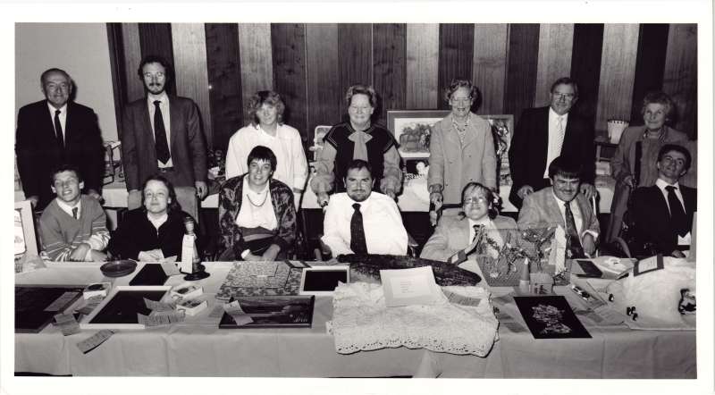 Group photograph of fourteen people sat at a table after receiving an award for their crafts