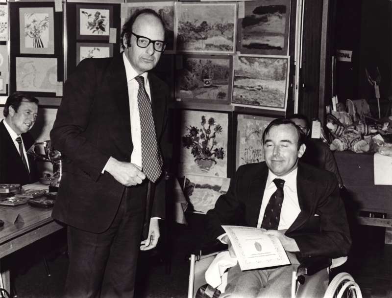 A man in a wheelchair receiving an award certificate for a painting