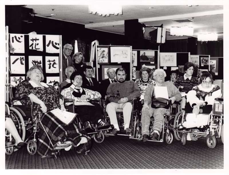 Group photograph of residents in wheelchairs holding various award certificates